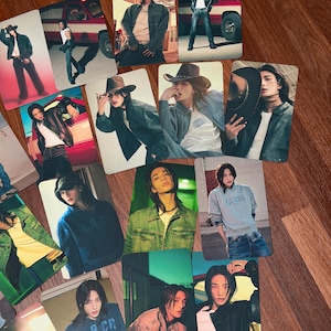 Può includere: Una collezione di cartoline fotografiche rettangolari che ritraggono una persona con lunghi capelli scuri in vari outfit, tra cui giacche di jeans, giacche di pelle, felpe con cappuccio e cappelli da cowboy, con un veicolo rosso sullo sfondo.