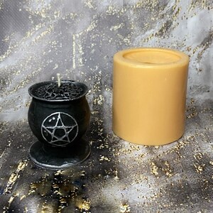 May include: A black cauldron candle with a pentagram design and a beige pillar candle. Both candles are on a grey and gold speckled surface.
