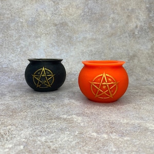 May include: Two small cauldron shaped candle holders, one black and one orange, with a gold pentagram design.