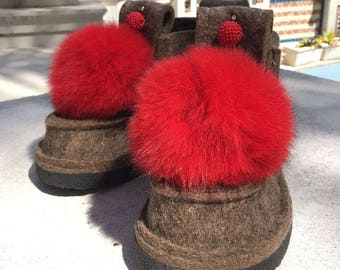 May include: Pair of brown felt boots with red fur pom-poms. The boots have a black rubber sole and a decorative red bead on each boot.