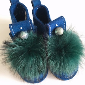 May include: A pair of blue felt slippers with green fur pom-poms and decorative blue and green buttons.