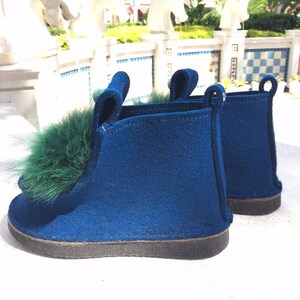 May include: A pair of blue felt slippers with a green fur pom-pom on one slipper.
