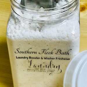 May include: A clear glass jar filled with white laundry booster powder. The jar has a black label that reads "Southern Fleek Bath Laundry Booster & Washer Freshener Laundry The Real Never Ending Story".