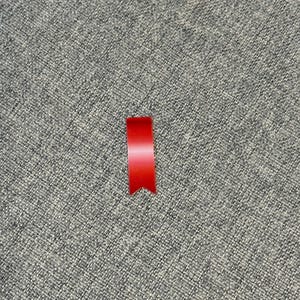 May include: A small, bright red ribbon with a pointed bottom edge. The ribbon is positioned vertically against a textured gray background, creating a simple yet striking contrast. The ribbon's color is vibrant and eye-catching.