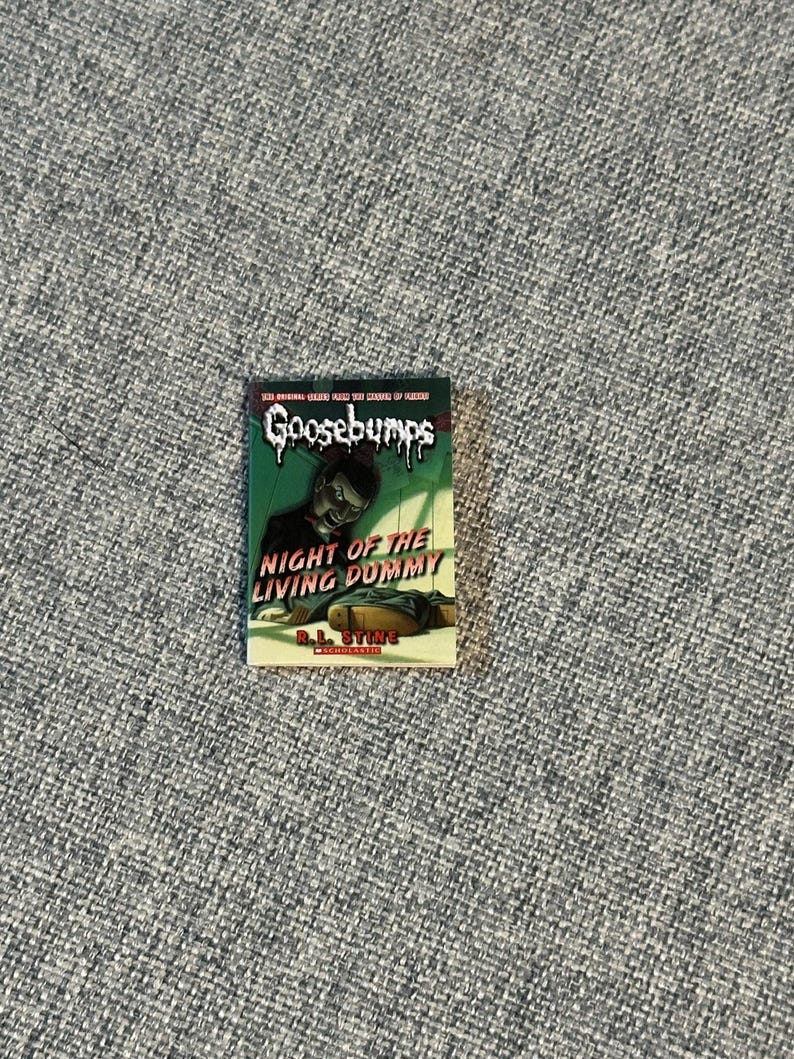 May include: A paperback book titled "Night of the Living Dummy" from the Goosebumps series. The cover features a green background with a menacing ventriloquist dummy and the Goosebumps logo. The author's name, R.L. Stine, is also visible.