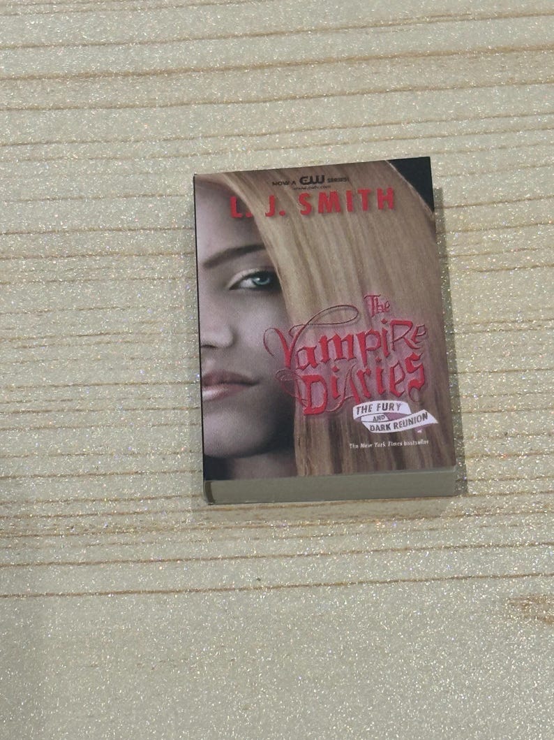 May include: A paperback book titled "The Vampire Diaries" by L.J. Smith. The cover features a woman's face with blonde hair and the title in red lettering. The book is a New York Times bestseller.