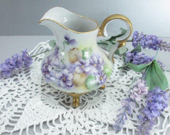 Jarra de crema antigua de porcelana pintada a mano con diseño de pensamientos morados y base dorada, estilo eduardiano, decoración floral rústica, principios del siglo XX.
