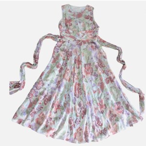 May include: A sleeveless floral dress with a flowing skirt and a matching waist tie. The dress features a pattern of red, purple, and pink flowers on a light green background. The dress is made of a lightweight fabric.