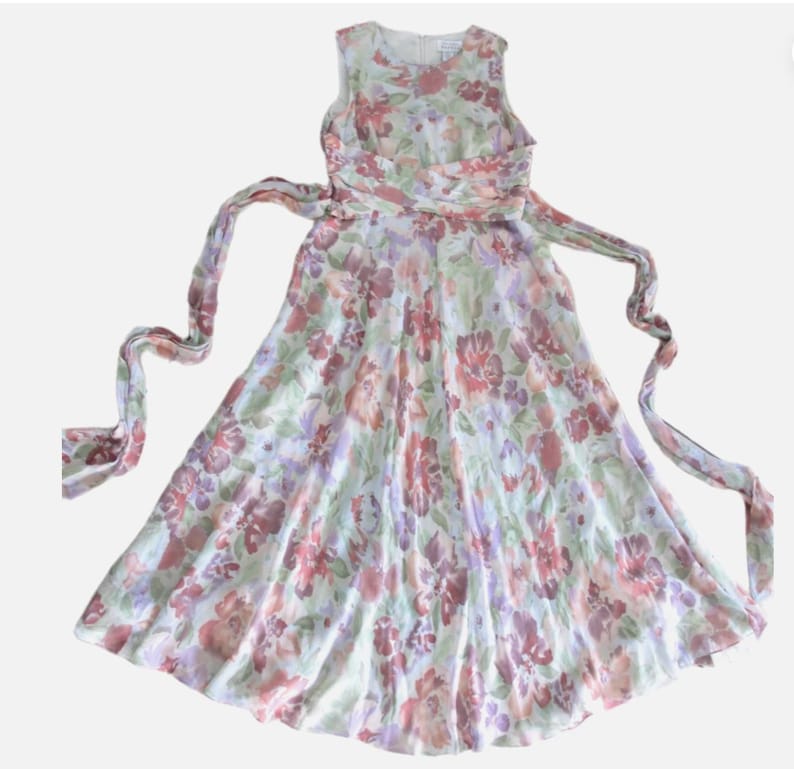 May include: A sleeveless floral dress with a flowing skirt and a matching waist tie. The dress features a pattern of red, purple, and pink flowers on a light green background. The dress is made of a lightweight fabric.