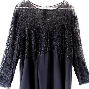 Puede incluir: Un vestido negro con mangas largas. La parte superior presenta un intrincado encaje con cuentas, mientras que la secci&oacute;n inferior es de tela oscura lisa. El vestido tiene un cuello redondo y una silueta fluida, adecuado para ocasiones formales.