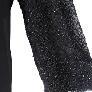 Puede incluir: Vestido negro con una manga adornada con abalorios. La manga es de tela transparente y est&aacute; cubierta con un intrincado patr&oacute;n de abalorios negros. El vestido en s&iacute; es de color negro liso, con la manga que proporciona un contraste decorativo.