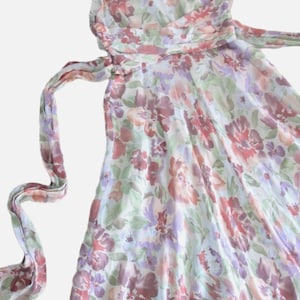 May include: A sleeveless floral print dress in shades of red, purple, and green on a white background. The dress has a flowing skirt and a matching sash that ties at the waist. The fabric appears to be lightweight.