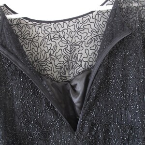 Puede incluir: Primer plano de un vestido negro con cuentas, con escote en V y cremallera. El vestido presenta intrincados patrones florales y un forro transparente bordado. El vestido est&aacute; colgado de una percha blanca.