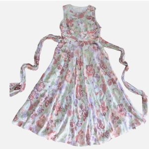 May include: A sleeveless floral dress with a flowing skirt and a matching waist tie. The dress features a pattern of red, purple, and pink flowers on a light green background. The dress is made of a lightweight fabric.