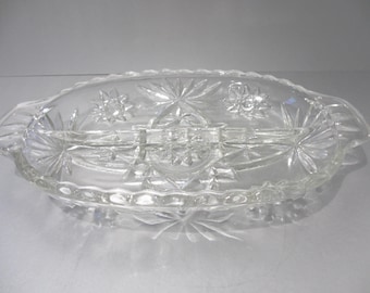 May include: Clear, oval-shaped glass serving dish with starburst and floral patterns. The dish is divided into three sections and features a scalloped edge and handles on each end. A decorative piece for serving.