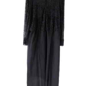 Puede incluir: Un vestido de noche negro con mangas largas. La parte superior del vestido est&aacute; cubierta con un material brillante y texturizado, mientras que la parte inferior es de tela lisa y fluida. El vestido tiene un escote redondo y una cremallera en la espalda. El dobladillo tiene un ribete blanco.