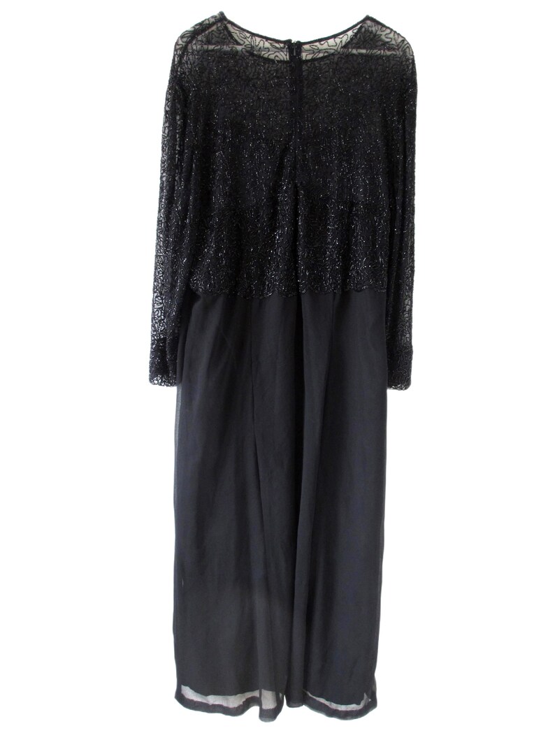 Puede incluir: Un vestido de noche negro con mangas largas. La parte superior del vestido est&aacute; cubierta con un material brillante y texturizado, mientras que la parte inferior es de tela lisa y fluida. El vestido tiene un escote redondo y una cremallera en la espalda. El dobladillo tiene un ribete blanco.