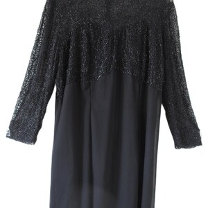 Puede incluir: Un vestido negro con mangas largas. La parte superior del vestido presenta un dise&ntilde;o detallado y texturizado con cuentas, mientras que la parte inferior es de tela lisa y fluida. El vestido cuelga de una percha blanca.