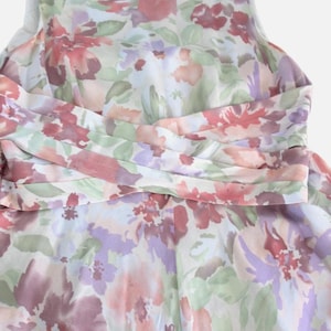 May include: A sleeveless floral dress featuring a watercolor-style print in shades of pink, purple, and green. The dress has a cinched waist detail and a flowing skirt. The fabric appears lightweight and suitable for warmer weather.