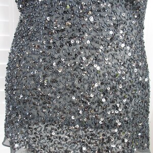 Puede incluir: Top gris oscuro, ricamente adornado con lentejuelas y abalorios. La prenda tiene un dobladillo transparente con volantes y est&aacute; cubierta de peque&ntilde;os adornos reflectantes. El top parece estar hecho de una tela ligera.