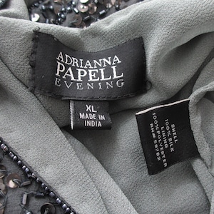 Puede incluir: Primer plano de un vestido gris Adrianna Papell Evening. La etiqueta dice "XL MADE IN INDIA". El vestido est&aacute; hecho de seda y poli&eacute;ster. El vestido est&aacute; adornado con lentejuelas y abalorios.