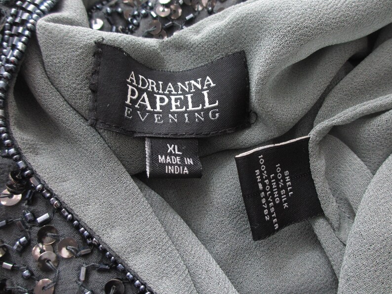 Puede incluir: Primer plano de un vestido gris Adrianna Papell Evening. La etiqueta dice "XL MADE IN INDIA". El vestido est&aacute; hecho de seda y poli&eacute;ster. El vestido est&aacute; adornado con lentejuelas y abalorios.