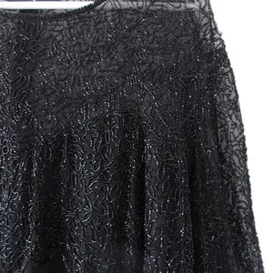 Puede incluir: Top de noche negro con intrincados patrones florales de cuentas. El top presenta un escote y mangas transparentes, con un dobladillo festoneado. El abalorio a&ntilde;ade textura y brillo a la prenda, creando un look elegante y sofisticado.