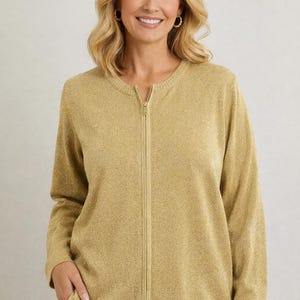 May include: A gold-colored zip-up sweater with long sleeves. The sweater has a round neckline and a full-length zipper. The fabric has a subtle shimmer. The person is wearing white pants. The sweater is a women's clothing item.