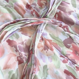 May include: A close-up of a floral patterned fabric in shades of pink, peach, and green. The fabric appears to be a lightweight material, possibly silk or a similar delicate weave. The design features a watercolor-like floral print.