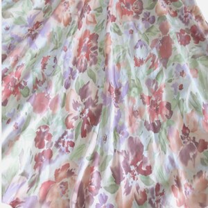 May include: A flowing fabric with a floral pattern in shades of red, purple, and peach. The design features large, stylized flowers and smaller blossoms on a white background. The fabric has a soft, delicate appearance.