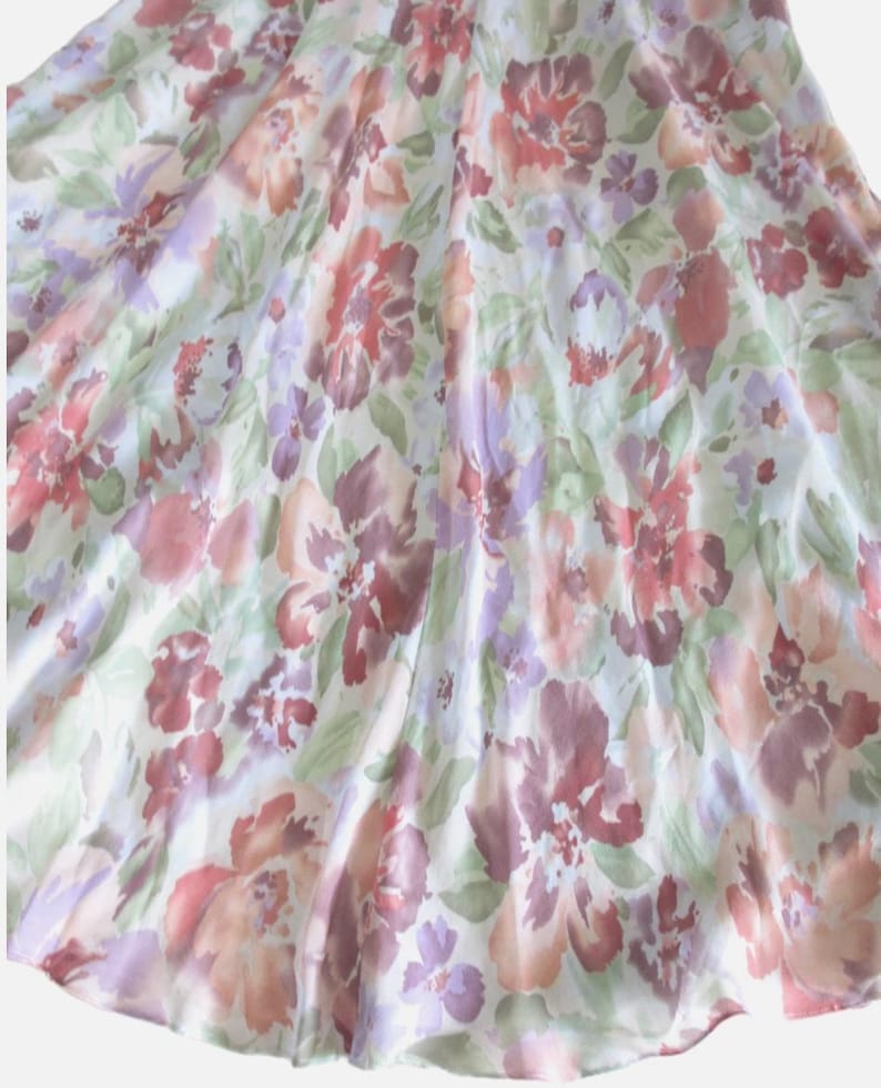 May include: A flowing fabric with a floral pattern in shades of red, purple, and peach. The design features large, stylized flowers and smaller blossoms on a white background. The fabric has a soft, delicate appearance.
