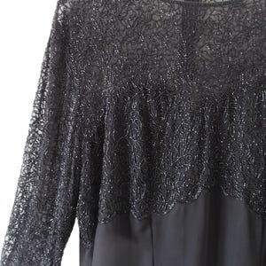 Puede incluir: Vestido de noche negro con mangas largas. La parte superior del vestido presenta intrincados detalles de cuentas, creando un efecto texturizado y brillante. Las mangas son transparentes y la falda es opaca.