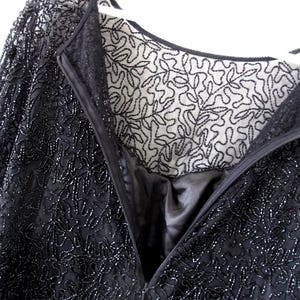 Puede incluir: Primer plano de un vestido negro con cuentas y un detallado estampado floral. El vestido presenta un escote en V profundo y cierre de cremallera. El forro es visible, mostrando una tela blanca contrastante con un dise&ntilde;o de hojas negras.