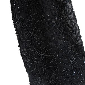 Puede incluir: Primer plano de una manga negra, ricamente adornada con intrincados abalorios. Las cuentas est&aacute;n dispuestas en un patr&oacute;n arremolinado, similar a flores, creando un dise&ntilde;o texturizado y elegante. La manga est&aacute; hecha de una tela negra transparente.