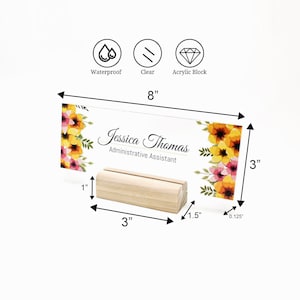 Puede incluir: Una placa de nombre de escritorio de acr&iacute;lico transparente con un dise&ntilde;o floral y el texto "Jessica Thomas, Asistente Administrativa". La placa mide 20,3 cm de ancho y 7,6 cm de alto. Se coloca sobre un soporte de madera de 7,6 cm de ancho.