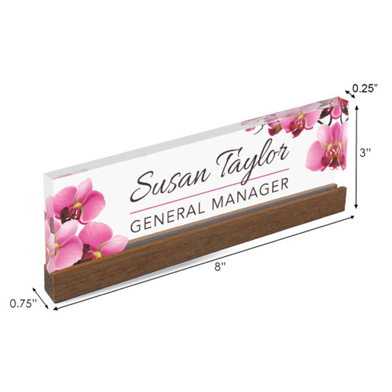 Puede incluir: Una placa de nombre de escritorio de acr&iacute;lico transparente con una base de madera. La placa de nombre presenta un dise&ntilde;o floral con orqu&iacute;deas rosas y el texto "Susan Taylor, General Manager". La placa de nombre mide 20,3 cm de largo, 7,6 cm de alto y 0,6 cm de grosor.