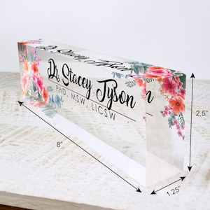 Puede incluir: Un porta-nombres de escritorio de acr&iacute;lico transparente con un dise&ntilde;o floral y el texto "Dr. Stacey Tyson, PhD, MSW, LICSW". El porta-nombres mide 20,3 cm de largo, 6,35 cm de alto y 3,175 cm de ancho.