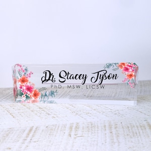 Puede incluir: Un porta-nombre de escritorio de acr&iacute;lico transparente con un dise&ntilde;o floral y el texto "Dr. Stacey Tyson, PhD, MSW, LICSW".