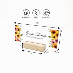 May include: A clear acrylic desk nameplate with a floral design and the text "Jessica Thomas, Administrative Assistant". The nameplate is 20.3 cm wide and 7.6 cm tall. It sits on a 7.6 cm wide wooden stand.