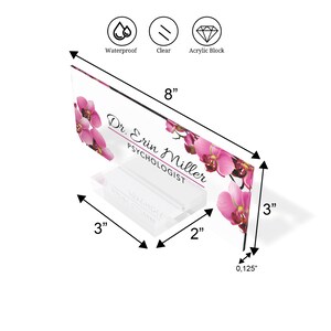 Może przedstawiać: Przezroczysty akrylowy stojak na biurko z r&oacute;żowym kwiatowym wzorem orchidei. Na stojaku widnieje napis "Dr. Erin Miller, Psycholog". Stojak ma 20,3 cm szerokości, 7,6 cm wysokości i 0,3 cm grubości.