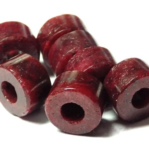 May include: A group of eight dark red round beads with a hole in the centre. The beads are made of a smooth, polished material.