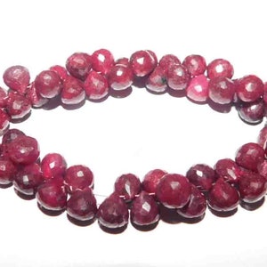May include: A strand of deep red ruby gemstone beads, each bead is faceted and has a teardrop shape. The beads are strung on a thin wire and are ready to be used for jewelry making.