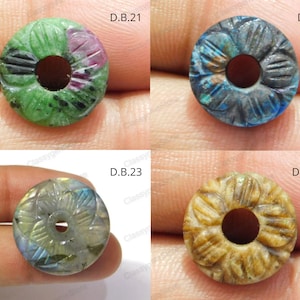 Può includere: Quattro perline di pietre preziose con disegni floreali scolpiti e un foro centrale. Le perline sono in vari colori: verde e rosa, blu, iridescente e marrone chiaro. Ogni perlina è etichettata con "D.B." seguito da un numero.