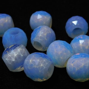 May include: A group of ten iridescent blue and white glass beads with a faceted design. The beads have a translucent appearance and are arranged in a cluster on a black background.