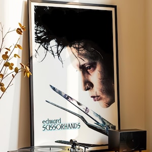 May include: A framed movie poster for "Edward Scissorhands" is displayed above a record player on a black and wood-tone cabinet. A vase with decorative branches and two small black vases are also visible.