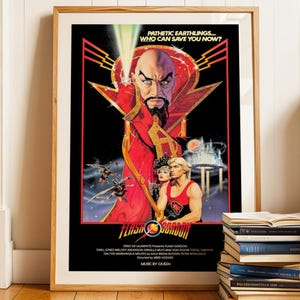 Op de afbeelding: Een ingelijste filmposter voor "Flash Gordon" met een centraal beeld van een streng kijkend personage in een rode mantel. De poster bevat de tekst "PATHETIC EARTHLINGS... WHO CAN SAVE YOU NOW?" en de filmtitel.