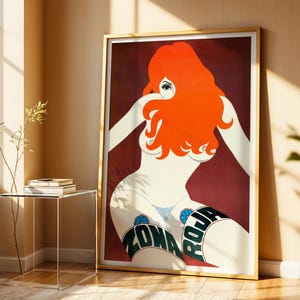 May include: A framed art print featuring a stylized illustration of a woman with vibrant red hair and a burgundy background. The artwork includes the text "ZONA ROJA" on the woman's thigh. The print is displayed in a room with natural light and a minimalist glass side table.
