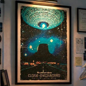 Könnte beinhalten: Ein gerahmtes Filmplakat von Unheimliche Begegnung der dritten Art mit einem leuchtenden UFO über einer Berglandschaft, in einem Forschungsbüro mit NASA-Tasse, einem Namensschild für Dr. E. Langford und Blick auf einen Planeten mit Ringen.