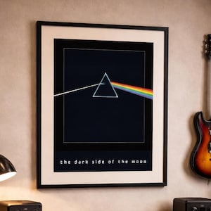 以下が含まれることがあります： 「The Dark Side of the Moon」のアルバムアートポスターが額装されたホームミュージックスタジオ。ラップトップ、スピーカー、ターンテーブル、キーボード、ギターが含まれています。デスクは濃い色の木材で作られています。