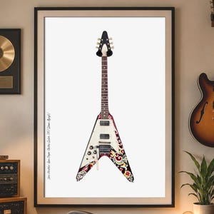 May include: A framed print of a white and red V-shaped guitar with a black headstock and intricate floral designs. The image is displayed in a music studio with other guitars, audio equipment, and a gold record.
